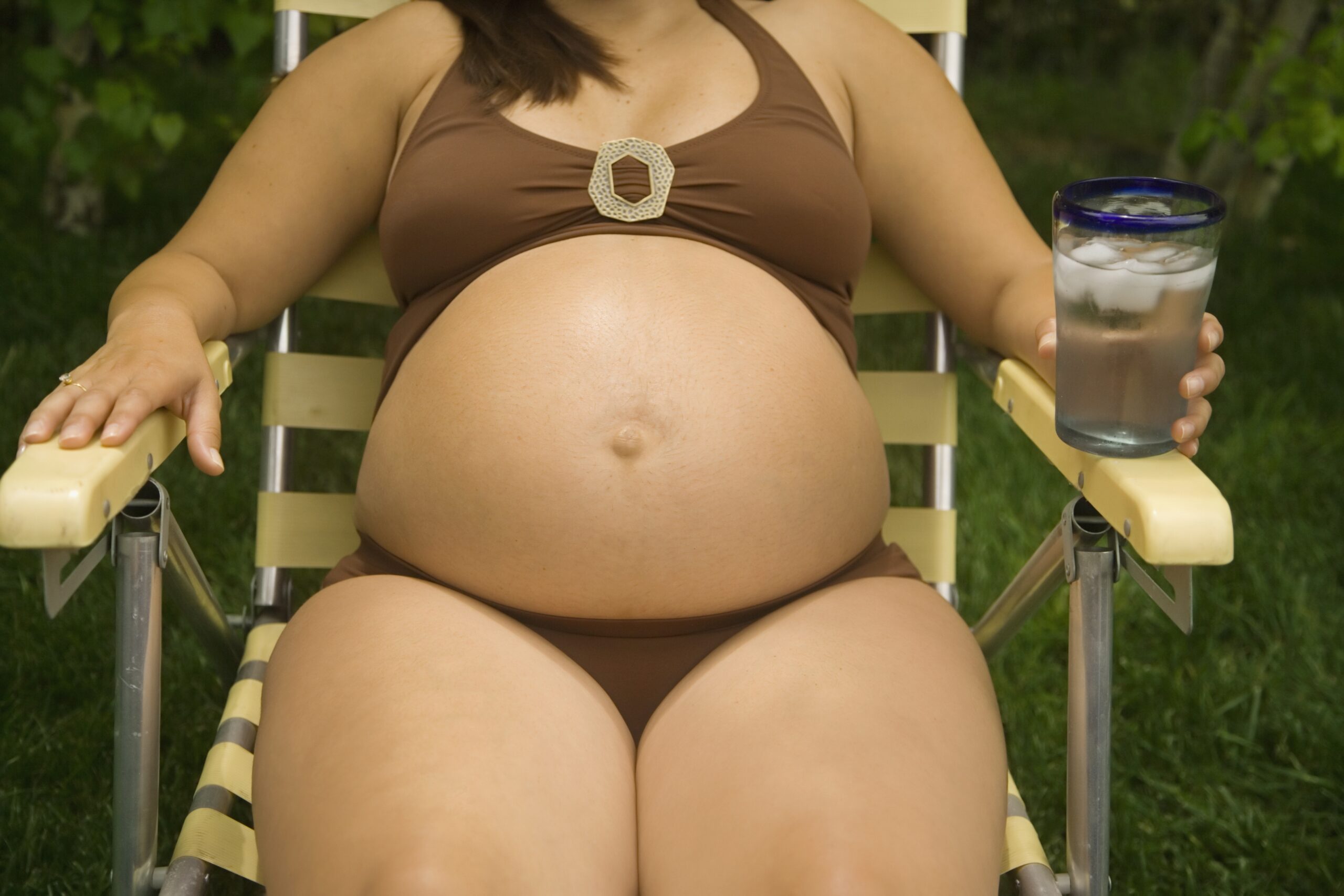 Pregnant woman laying in lawn chair wearing bathing suit